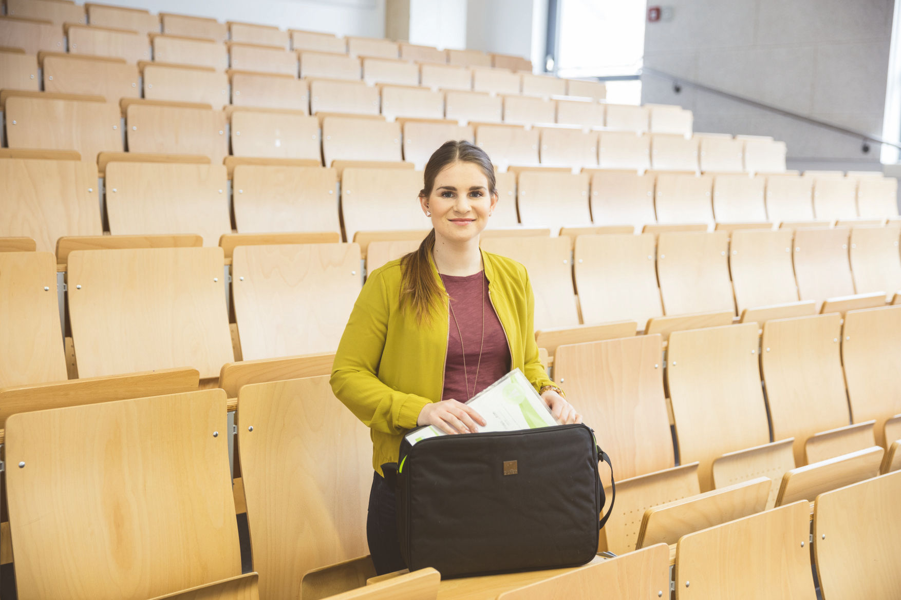 Studentin steht in einem leeren Hörsaal und packt Unterlagen in ihre Tasche